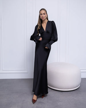 Woman in a black evening gown standing against a white paneled wall.