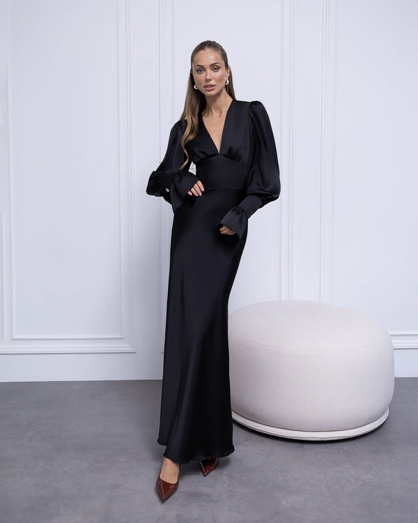 Woman in a black evening gown standing against a white paneled wall.