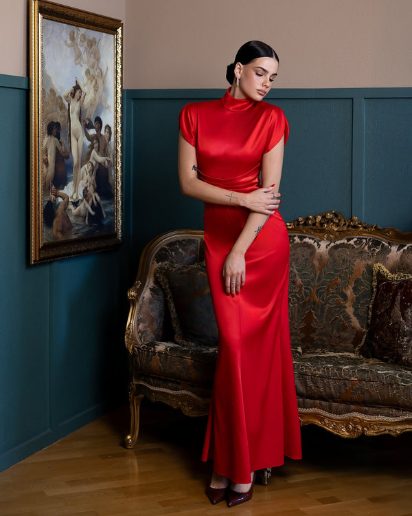 Woman in a red dress standing in a room with a painting and ornate sofa.