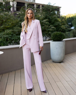 Woman in a pink suit standing on a wooden deck with greenery in the background