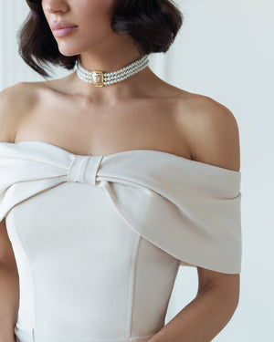Woman wearing a white off-shoulder dress with a large bow detail on a plain background