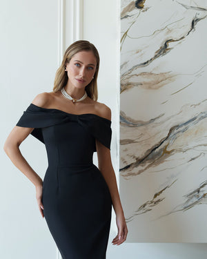 Woman in a black off-shoulder dress standing against a marble wall.